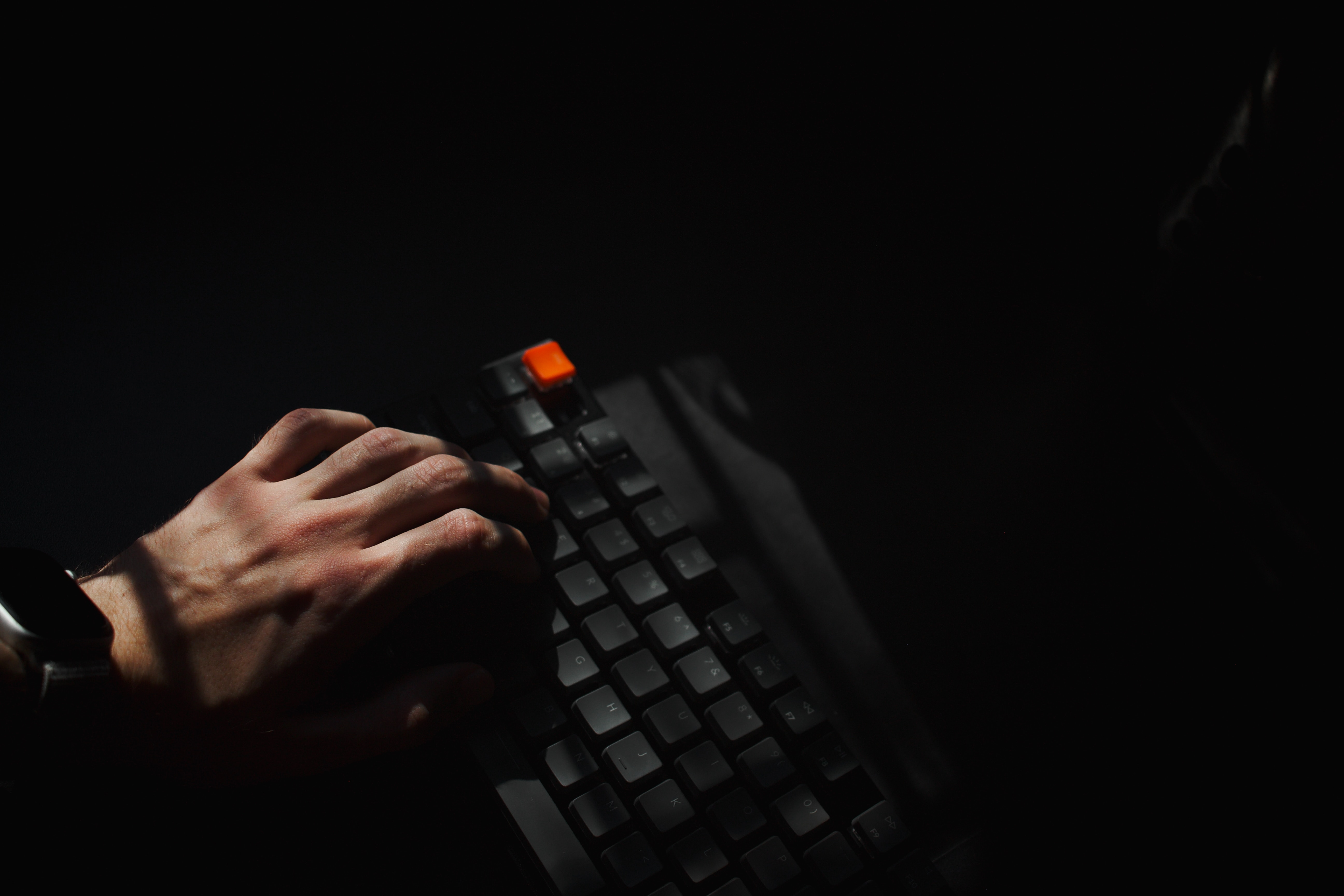 Hand typing on a keyboard in dark space with orange ESC button, photo credit to Quinton Coetzee